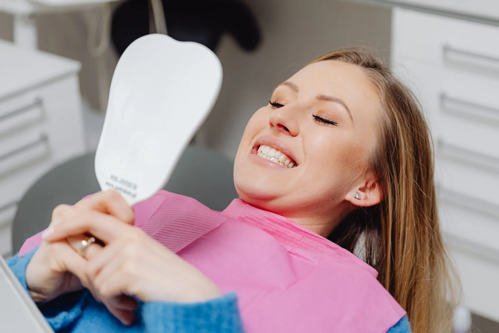 A woman smiling at her teeth in a hand mirror after treatment